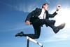 Man in suit jumping over hurdle on running track