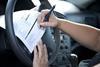 A man signing paperwork on steering wheel of car