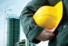 A man holding a hard hat with construction in the background