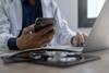 Doctor using mobile smartphone working on laptop computer in medical office Close the teleconference telemedicine
