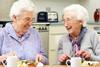 Two older women eating roast dinner with cups of tea, laughing