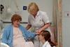 Two nurses helping an older lady from her hospital bed