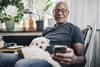 capita-photography-stock-original-getty1151007843-smiling-retired-senior-male-using-smart-phone-while-sitting-with-dog-in-room-at-home (1)
