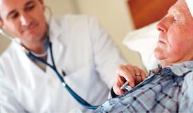 Older man in bed with health worker tending to him