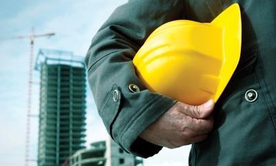 A man holding a hard hat with construction in the background